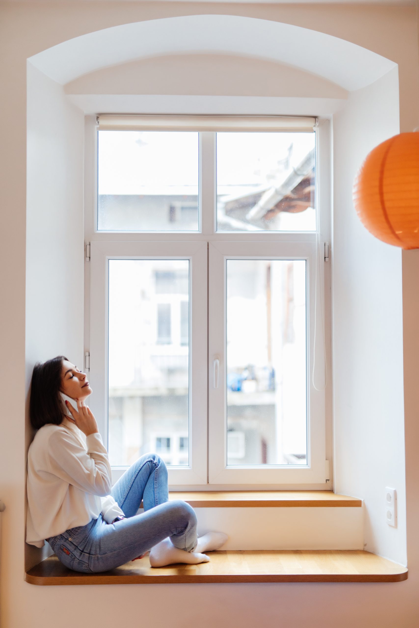 happy woman is talking on phone while sitting near the window